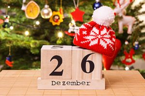 Stefanitag: Datum auf Holzwürfel mit einer roten weihnachtlichen Wollmütze oben drauf und einem geschmückten Weihnachtsbaum im Hintergrund mit Lichtern