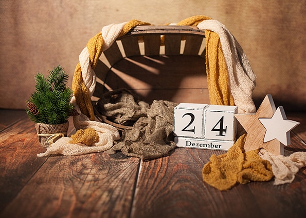 Kalenderdatum und Holzkiste mit Tuch auf einem Holzboden mit Weihnachtsdekoration (Sterne und kleiner Christbaum)